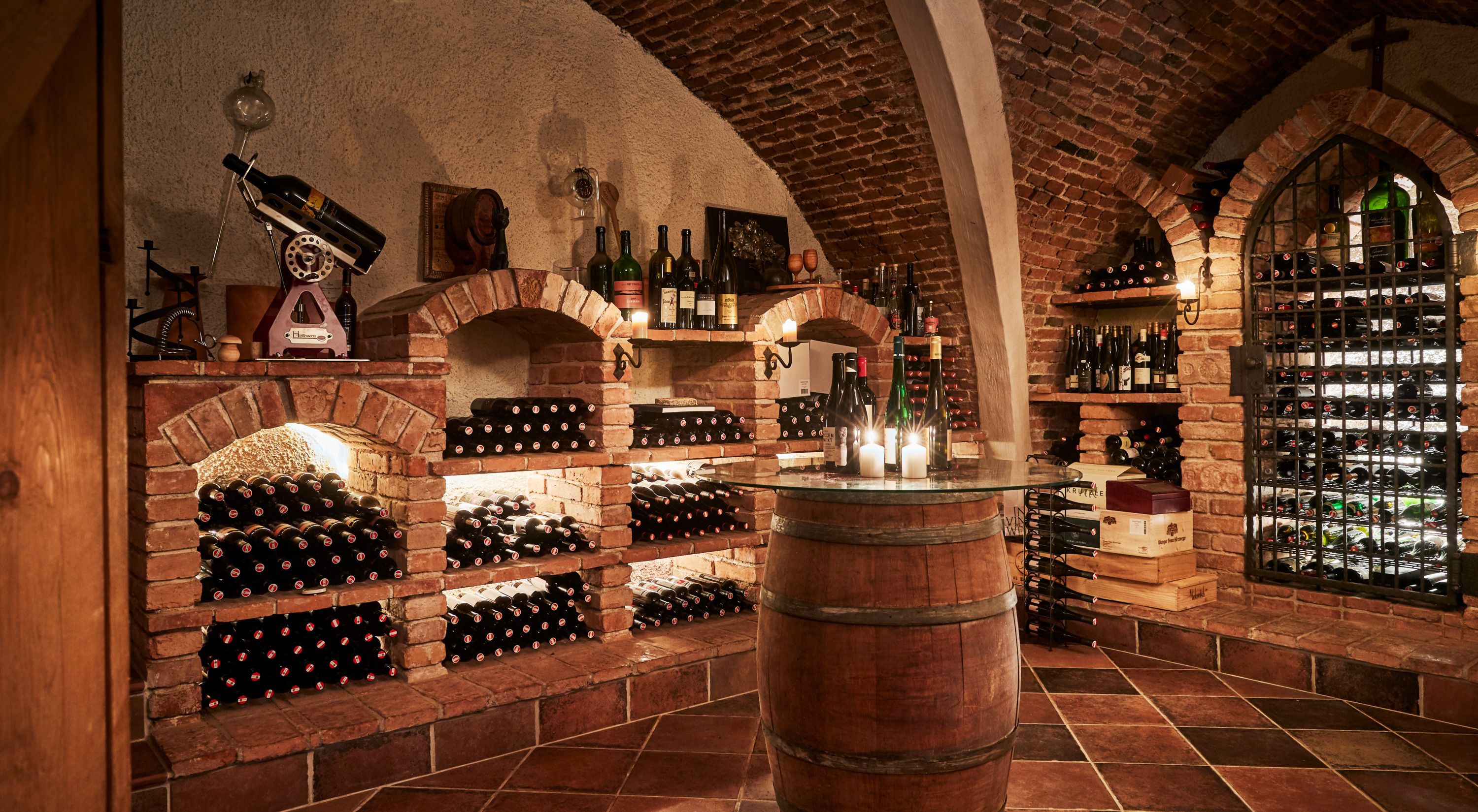 Historic wine cellar with brick vaults, wine bottles on shelves and candles on a barrel.