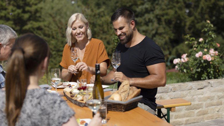 Group of people sitting at an outdoor table enjoying wine and bread.