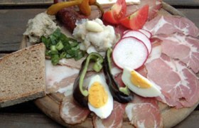 A traditional board with various types of sausage and cheese, bread, eggs and vegetables.