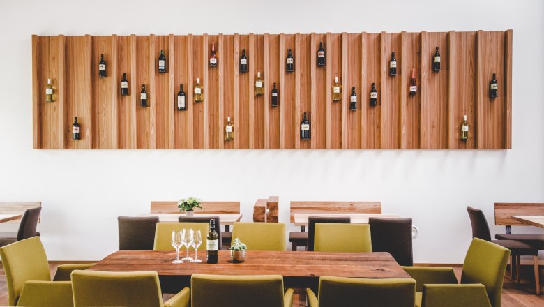 Interior view of a modern wine tavern with wooden tables and wine bottles on the wall.