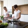 Two women cooking in a modern kitchen with fresh vegetables on the worktop.