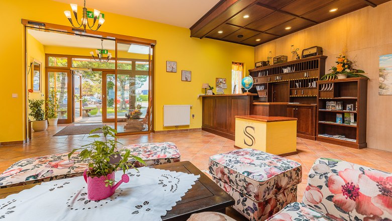 Hotel reception with yellow walls, wooden furniture and floral pattern armchairs.