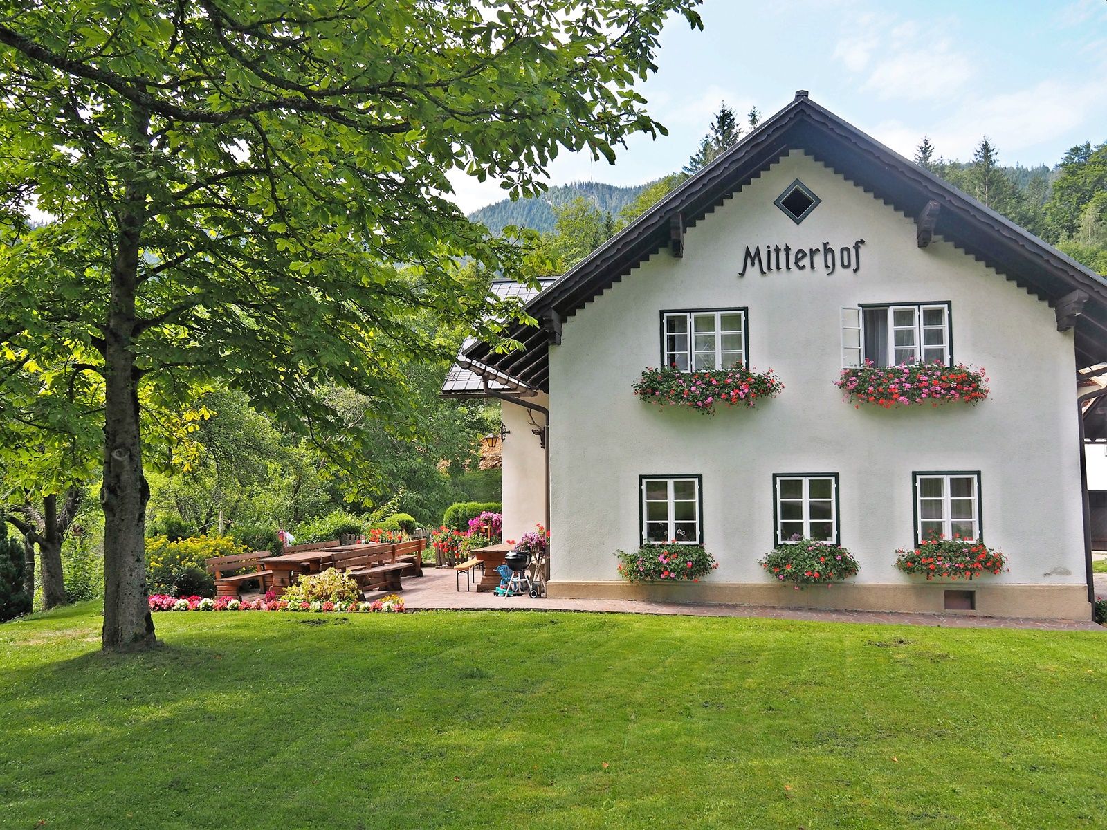 A traditional farmhouse called Mitterhof, surrounded by green countryside and flowerbeds.