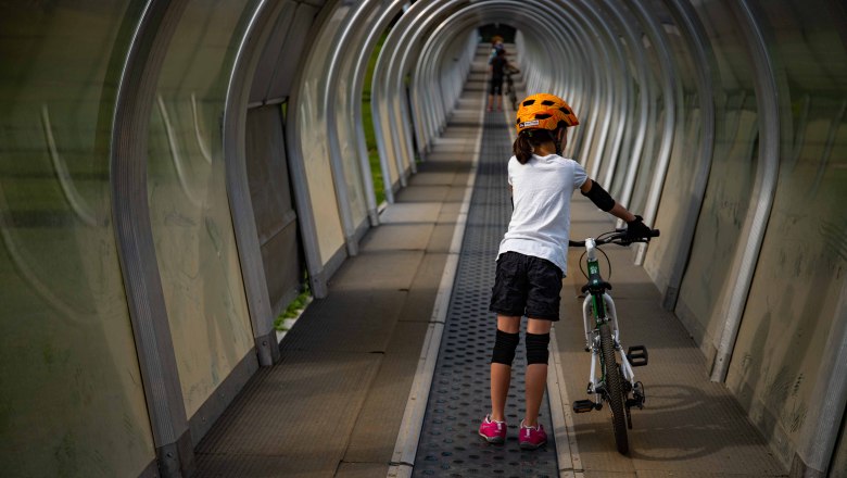Child with bicycle on conveyor belt in covered tunnel.