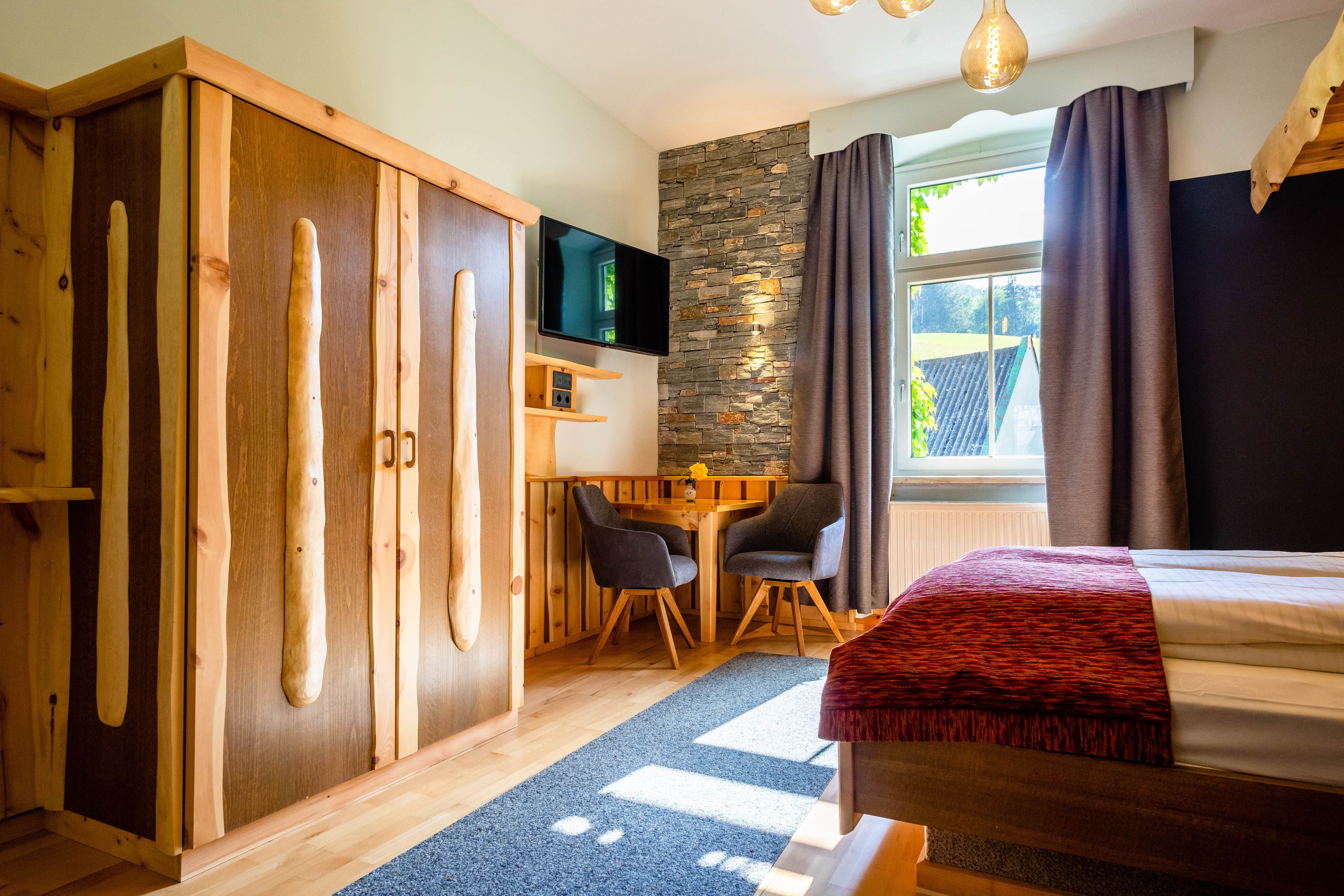 Cozy room with wooden furniture, stone wall, table and chairs, TV and window with curtains.