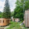 Three small wooden houses in a green forest landscape.