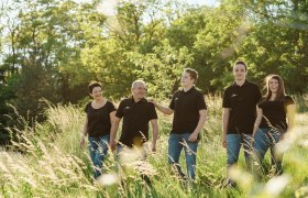 A smiling family strolls through a green meadow in the sunshine.