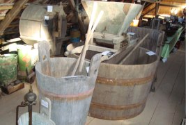 Interior view of a museum with old agricultural equipment and wooden vats.