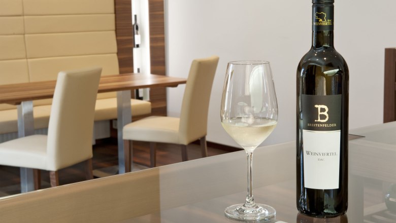 A tasting room with a bottle of white wine and a filled wine glass on a table.