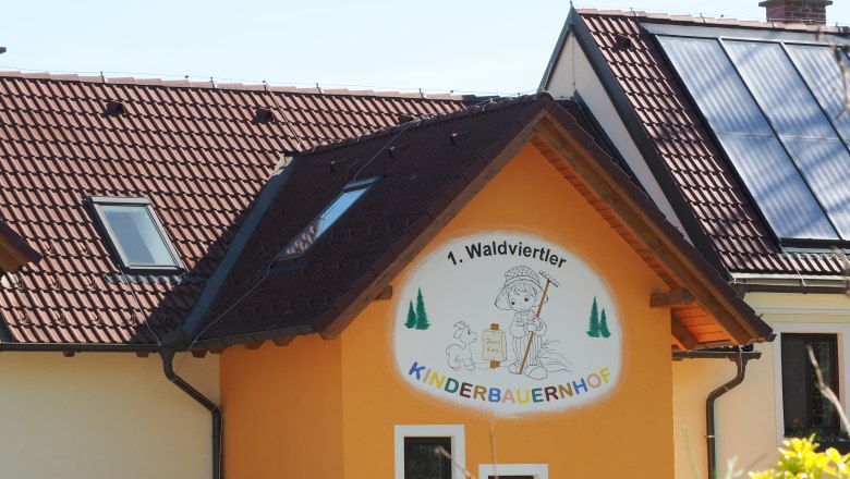 Building with sign '1. Waldviertler Kinderbauernhof', solar panels on the roof.