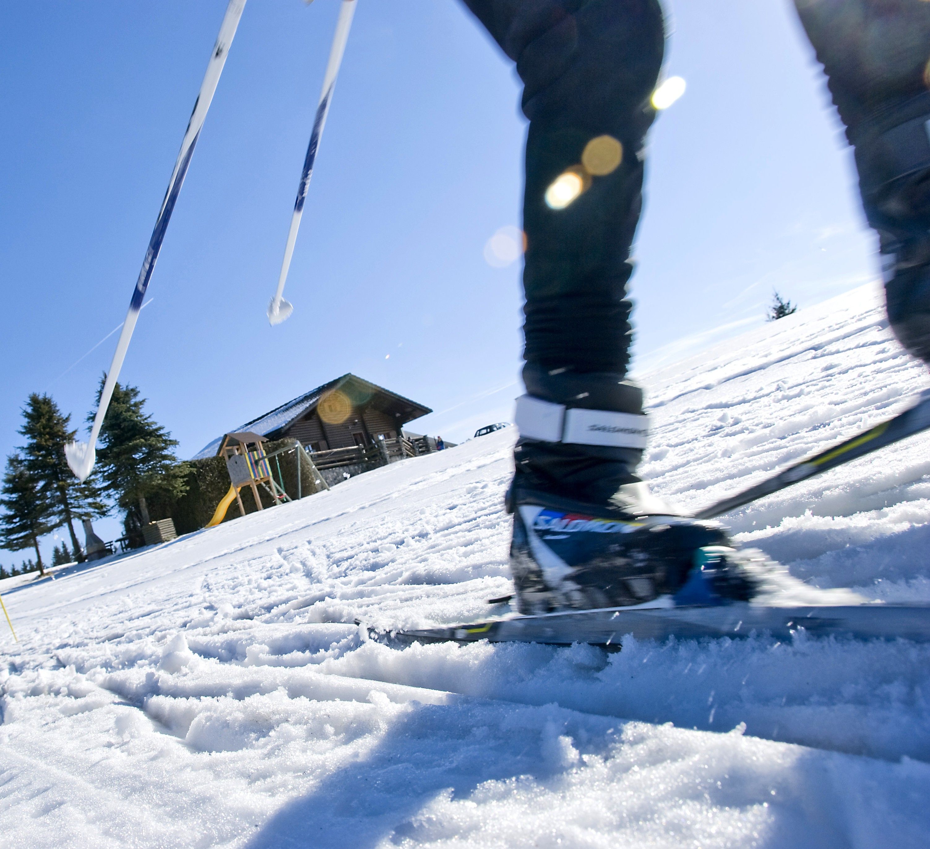Close-up of a cross-country skier on a snow-covered slope with a wooden hut in the background.