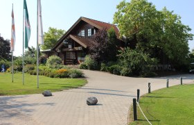 Entrance of a golf club with wooden building and flags.