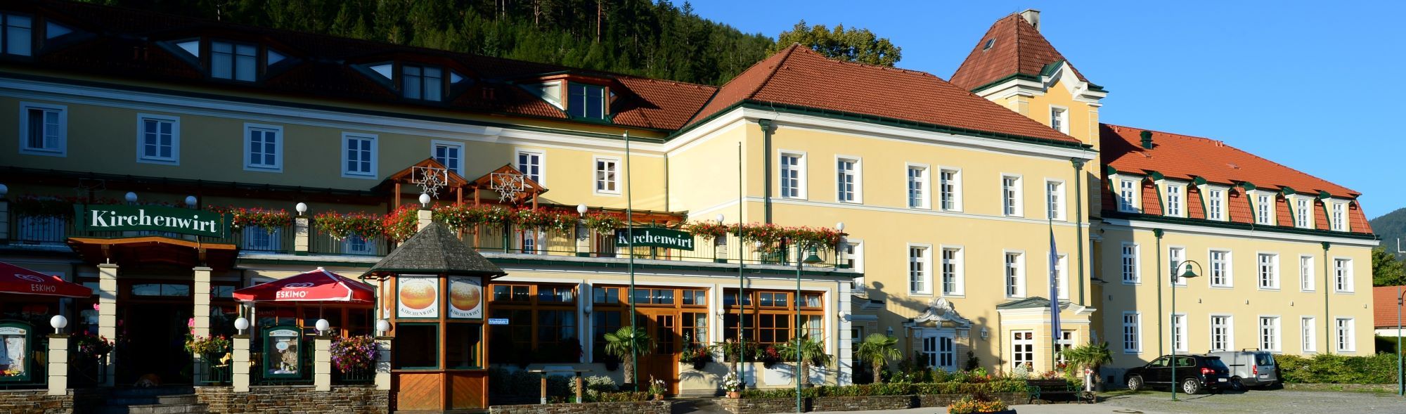Exterior view of a yellow building with red roofs and the sign 'Kirchenwirt'.
