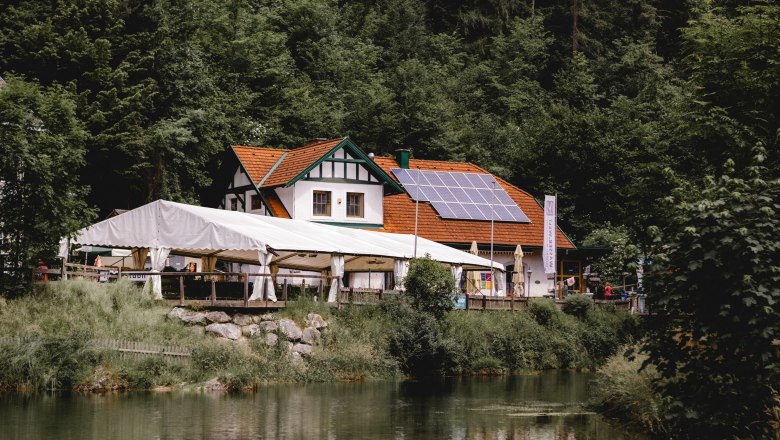 Inn with solar panels and tent on the edge of the forest, near a pond.