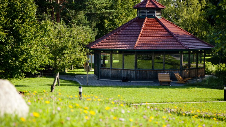 A pavilion with a red roof in a green park, surrounded by trees and flowers.
