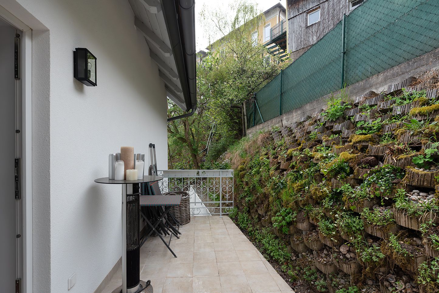 Terrace with table and chairs next to a green wall.