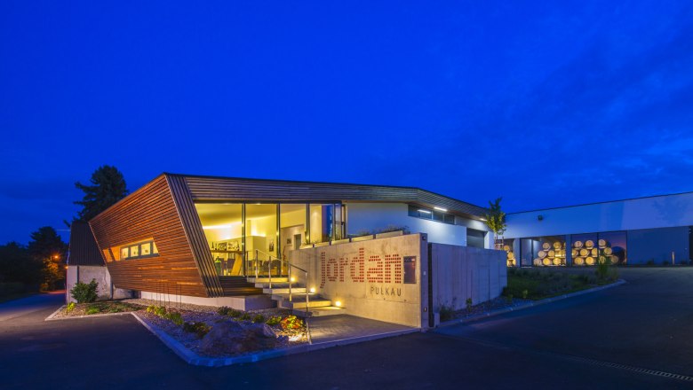 Modern winery at night with illuminated entrance and wooden paneling.