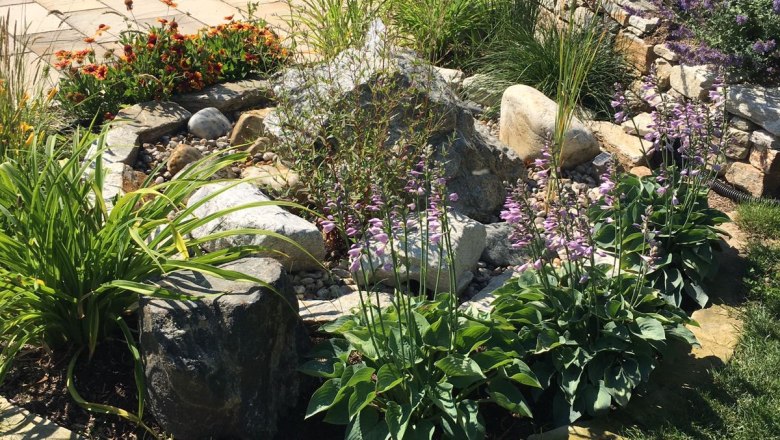 Garden with stone wall, bench and flower bed.