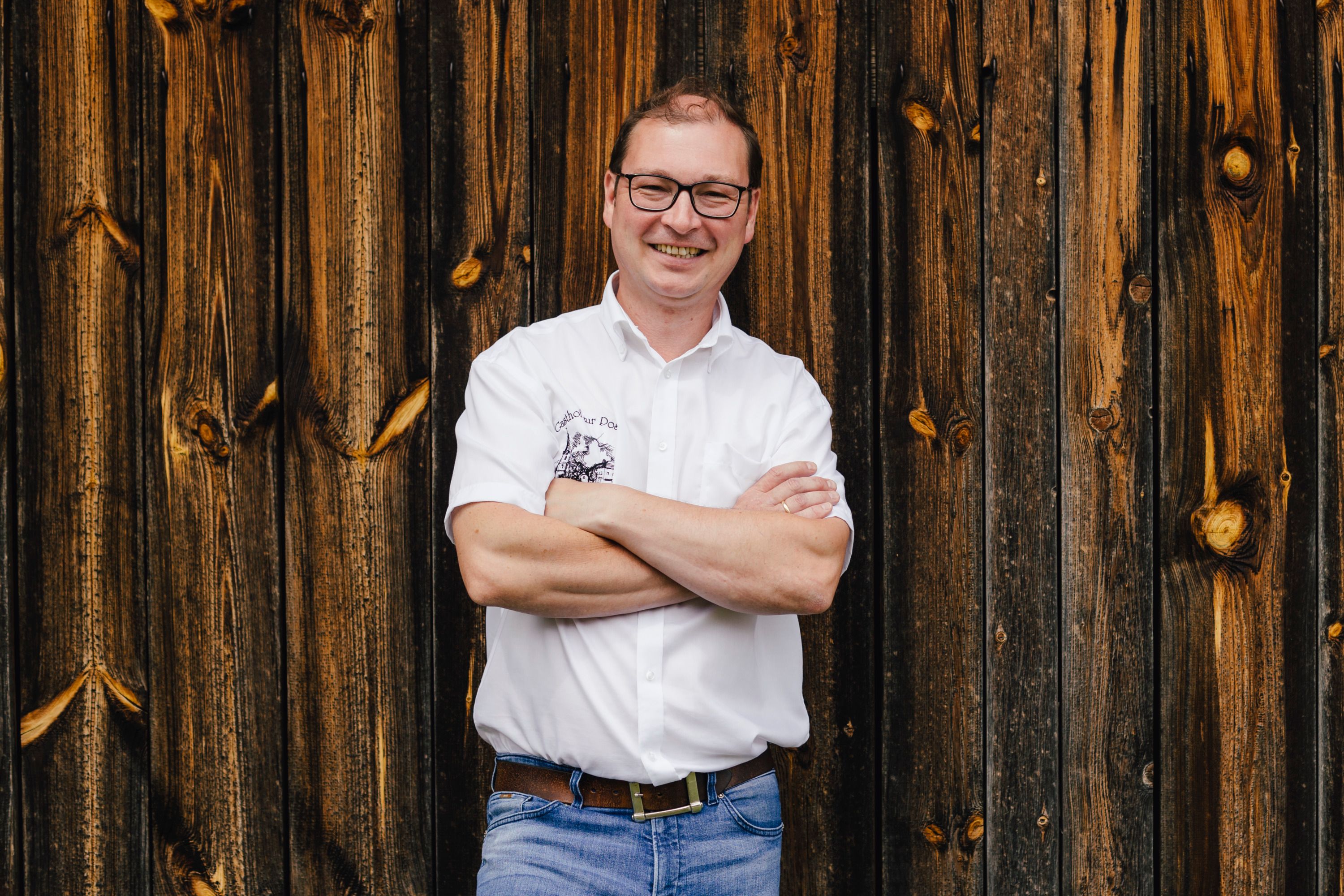 Man in white shirt in front of wooden wall.