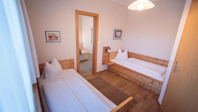 Two single beds in a cozy room with wooden furniture and pictures on the walls.