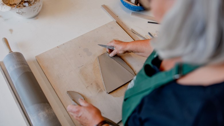 Person cutting clay on a table with a knife, surrounded by pottery tools.