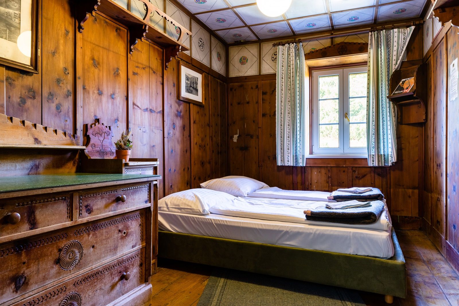 Rustic double room with wooden walls, a bed and a chest of drawers.