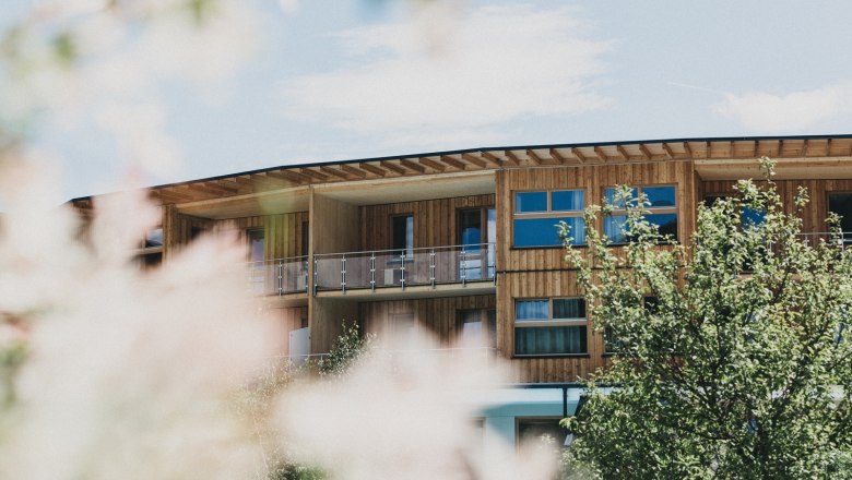Wooden building of the Naturhotel Molzbachhof with trees in the foreground.