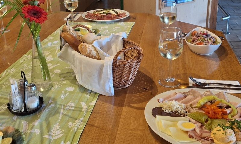A laid table with a platter of cold meats and cheese, bread basket, salad and wine glasses.