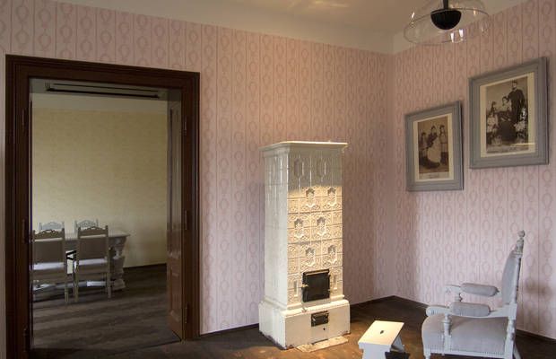 Interior view of a room with an antique stove, two framed pictures and a chair.