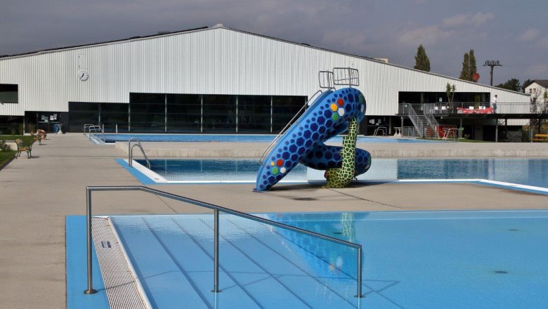 An empty outdoor pool with a colorful slide and a large building in the background.