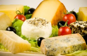 Various cheeses on a wooden board with tomatoes and olives.
