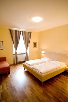 Double room, © ©Gasthaus Ludl A cozy double room with a large bed, wooden floor, an armchair and a window with curtains.