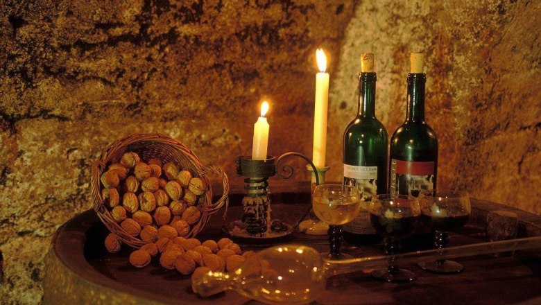 A wine cellar with candlelight, two bottles of wine, glasses and a basket full of walnuts on a barrel.