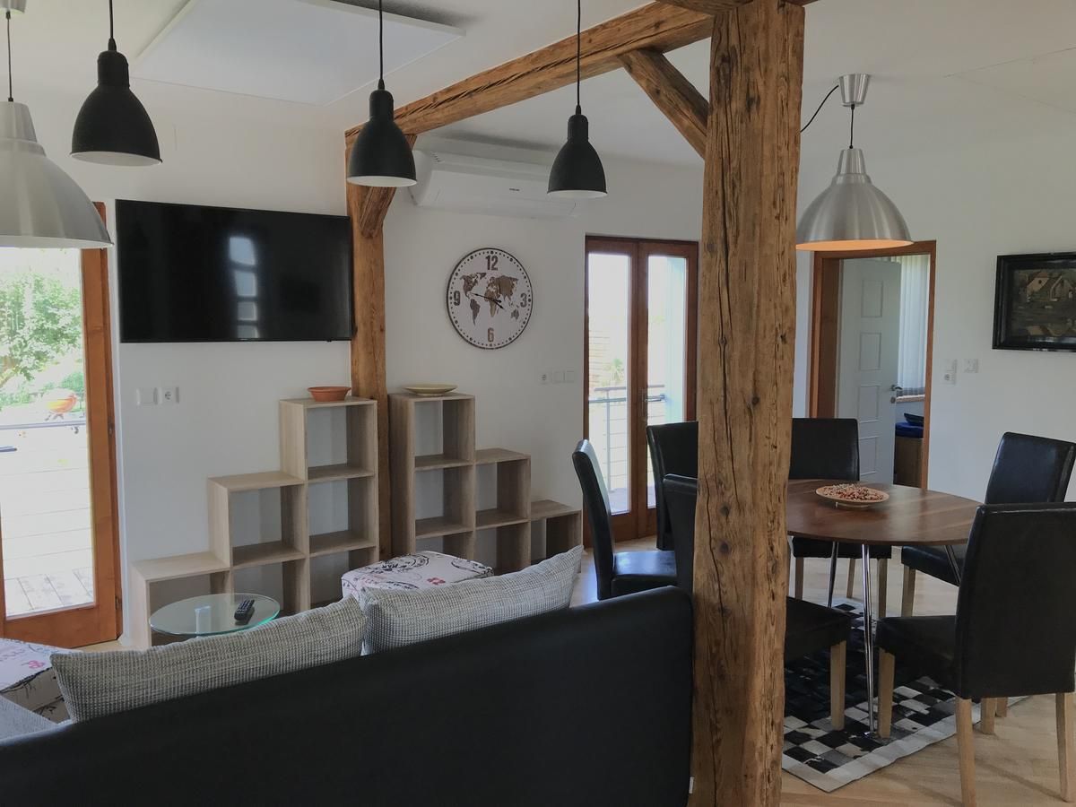 Modern living area with wooden beams, dining table, chairs, wall shelf, clock and TV.