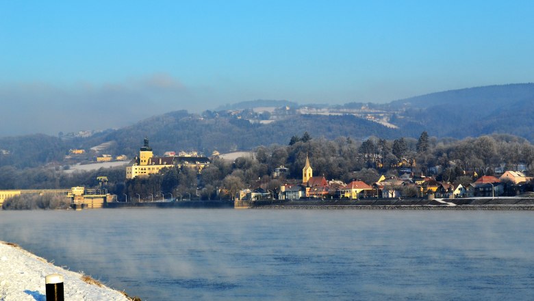 Winter landscape in Persenbeug with river, buildings and hills in the background.