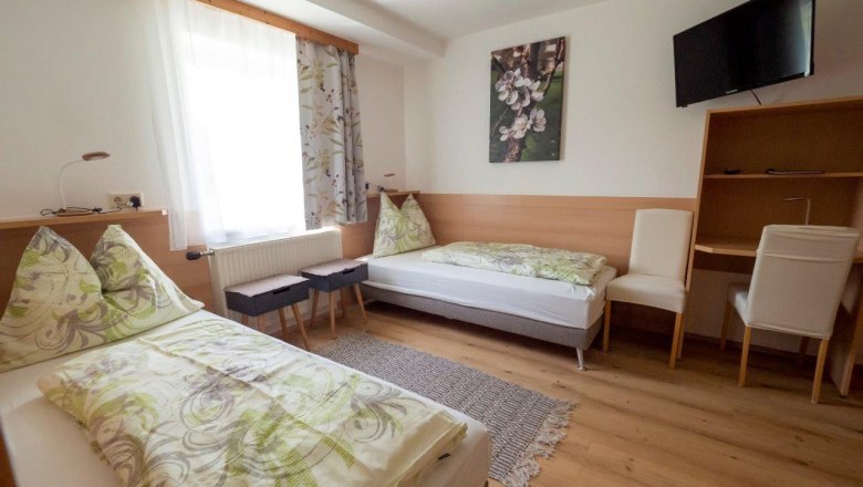 Cozy guest room with two single beds, a desk, chairs and a TV on the wall.