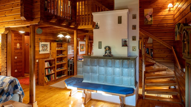 Cozy living room with tiled stove, wooden walls and staircase.