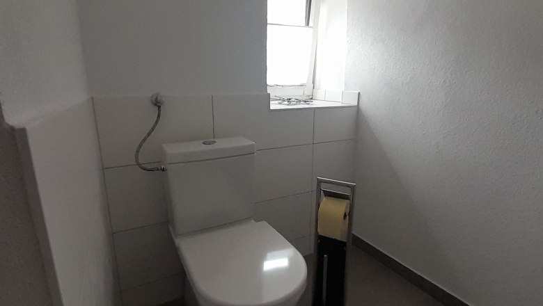 A simple bathroom with toilet, toilet paper holder and small window.