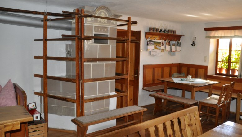 Interior view of a traditional farmhouse with tiled stove and wooden furniture.
