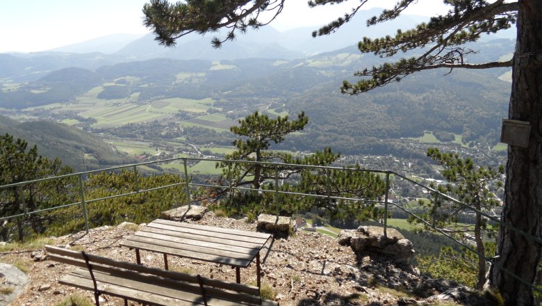 Viewpoint with bench and table, surrounded by trees, with a view of a valley and mountains in the background.
