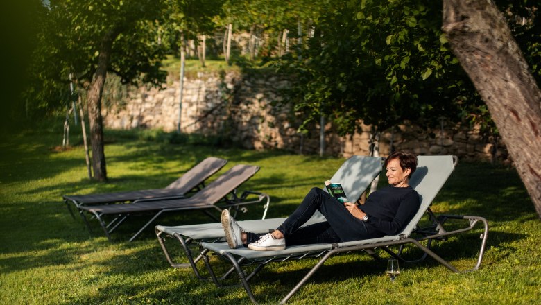 Person reads on a sun lounger in the garden.