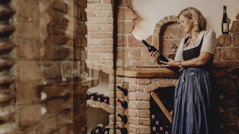 Woman in traditional dress holding a wine bottle in a rustic wine cellar.