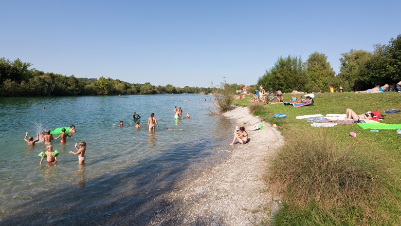 People swimming and relaxing at Lake Ratzersdorf on a sunny day.