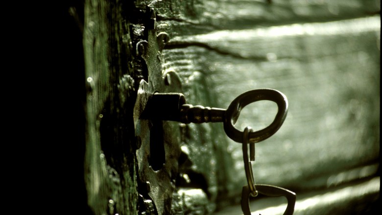 An old key is stuck in an antique lock on a wooden door.