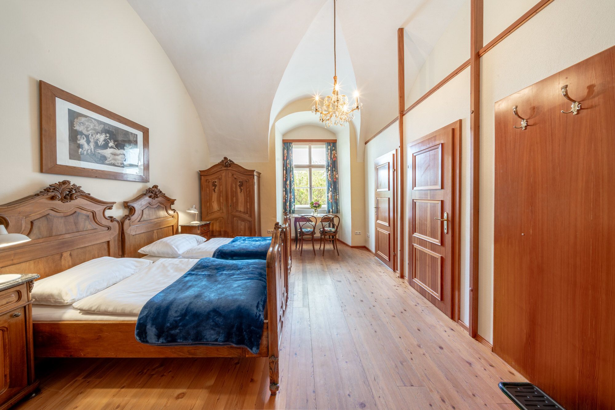 An elegant double room with antique wooden furniture, a chandelier and a window with a view of the greenery.