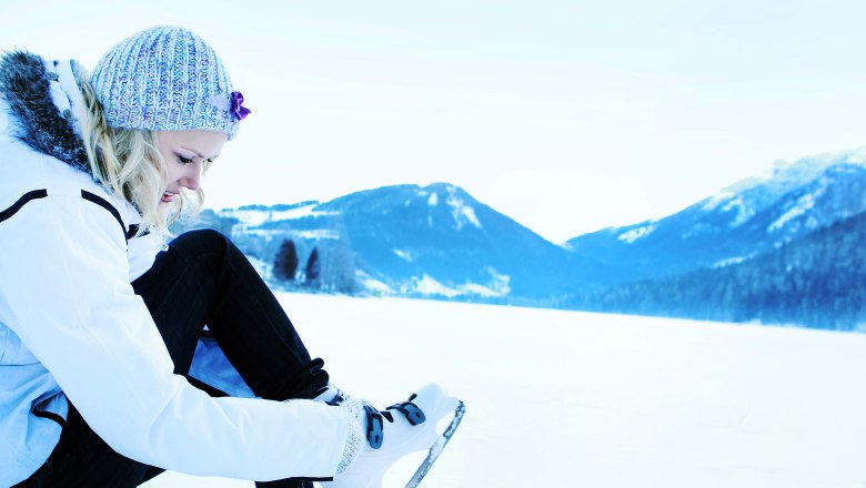 Person puts on ice skates on a snowy lake surrounded by mountains.