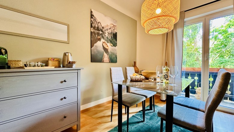 Cozy dining room with table, chairs and hanging lamp, view of balcony and nature.