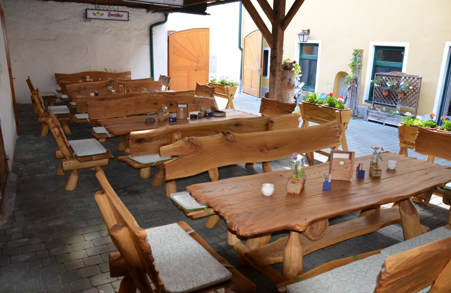 Rustic wooden benches and tables in an inn courtyard with flowers and decorations.