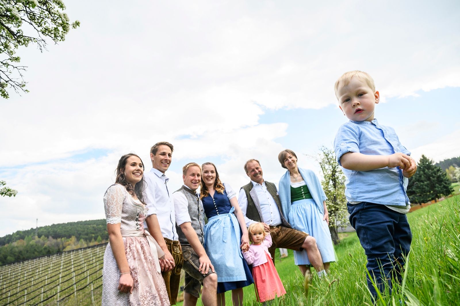 A family in traditional dress stands in a meadow, a small boy in the foreground.