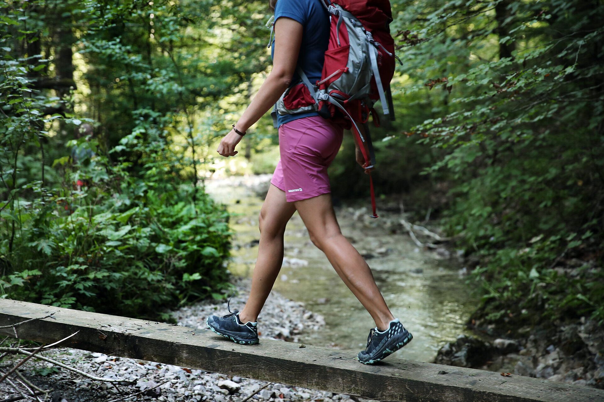 Woman in hiking outfit balancing on wooden posts over a small stream. 